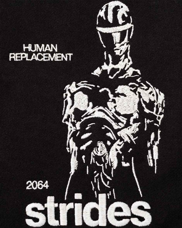 Nahaufnahme von dem STRIDES 2064 EMBROIDERY HOODIE in schwarz. Zu sehen ist ein eingestickter "HUMAN REPLACEMENT" Schriftzug, einen Robot/Figur und ein "2064 - Strides" Schriftzug.